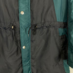 Close-up of a black and teal 1992/93 Ajax bench coat by Umbro, showcasing buttons and drawstrings at the waist.