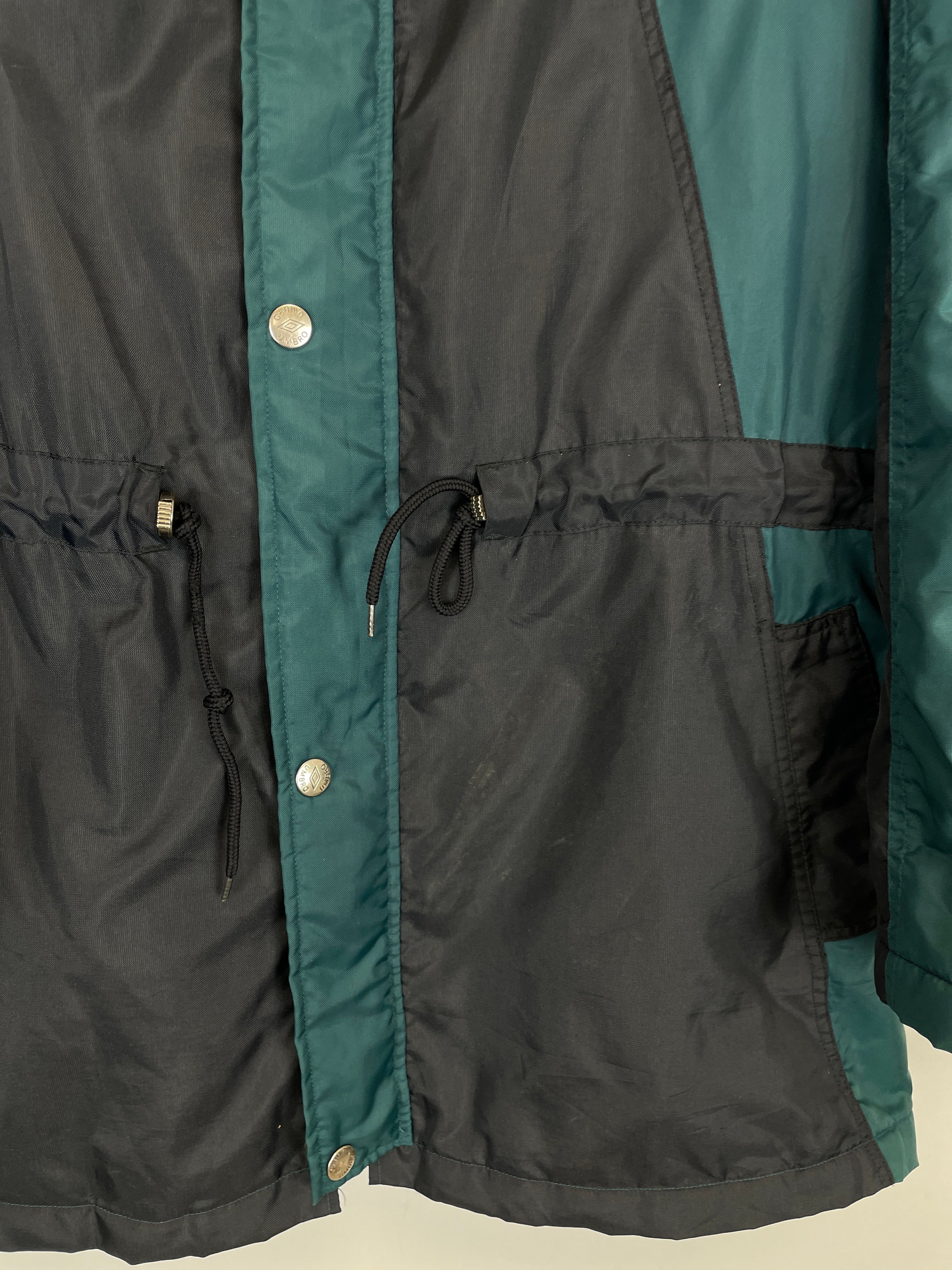 Close-up of a black and teal 1992/93 Ajax bench coat by Umbro, showcasing buttons and drawstrings at the waist.